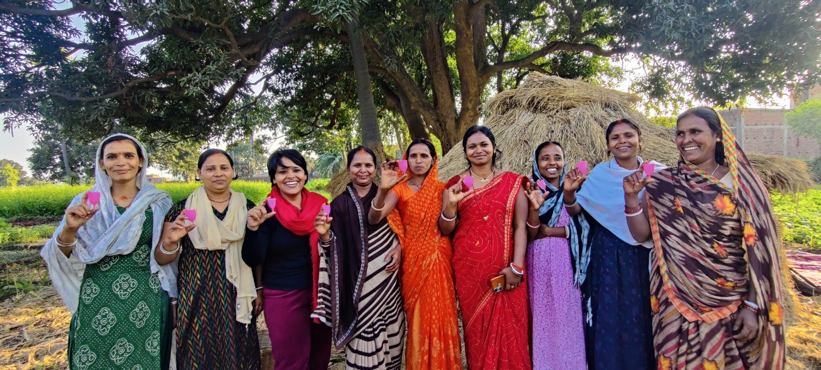 Community women holding pink menstrual cups outdoors